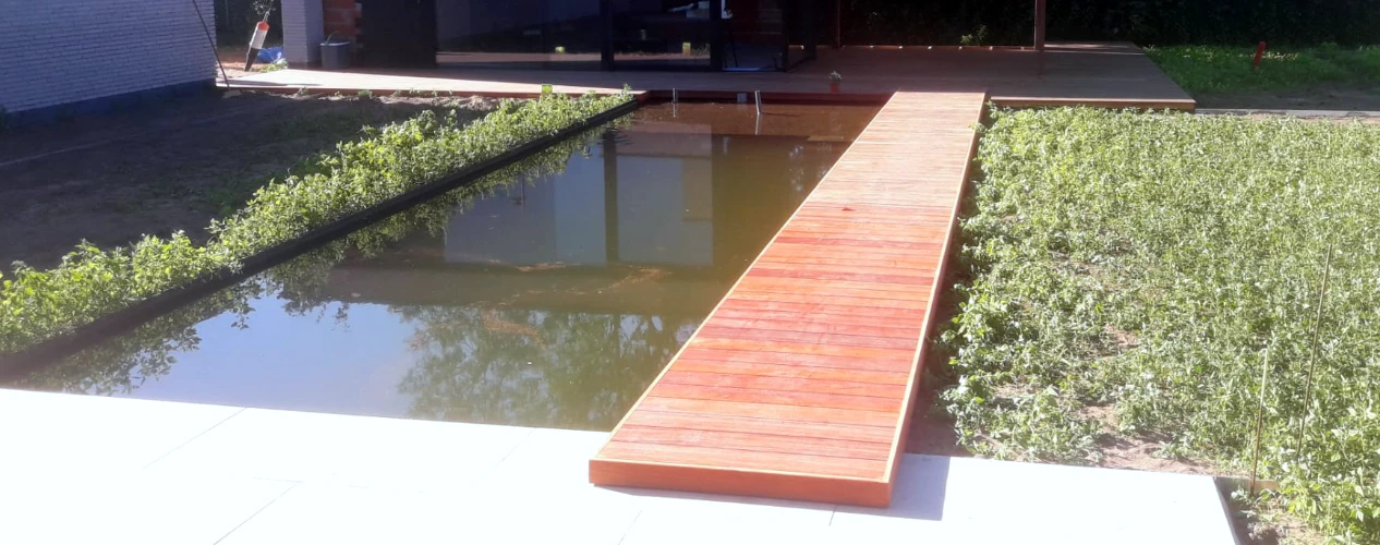 Houten terras op maat met loopplank over vijver in het Meetjesland